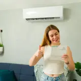 Uśmiechnięta kobieta z kciukiem w górze cieszy się z dokumentu, który może oznaczać dofinansowanie do klimatyzacji.