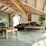 Nowoczesny salon z drewnianym sufitem i posadzką żywiczną w domu. Skórzane kanapy, drewniane stoliki i rośliny tworzą przytulną atmosferę.