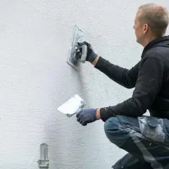 Murarz tworzy unikalne tynki strukturalne wzory na ścianie, nadając jej nowoczesny wygląd.