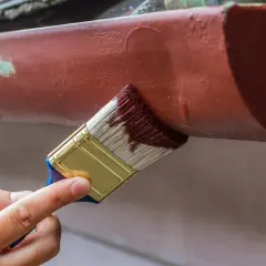 Ręka maluje pędzlem rynny, odnawiając stare malowanie aluminium.