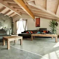 Nowoczesny salon z drewnianym sufitem i posadzką żywiczną w domu. Skórzane kanapy, drewniane stoliki i rośliny tworzą przytulną atmosferę.