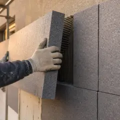 Ręce w rękawicach montują płyty z grafitowego styropianu na elewacji. To dobry wybór, jaki styropian na elewację wybrać, by zapewnić izolację.
