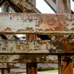 Metalowe belki konstrukcji pokryte łuszczącą się farbą i rdzą. Widać ślady postępującej korozji, która niszczy materiał.