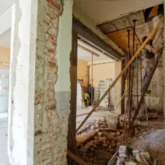 Remont starego domu: pracownicy na drabinach, gruz i materiały budowlane. Widać postęp prac nad tym, jak wyrównać ściany w starym domu.
