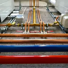 Instalacja hydrauliczna z miedzianymi rurami, zaworami i niebieską/czerwoną rurą. Ocieplenie rury wodnej jest kluczowe dla efektywności systemu.