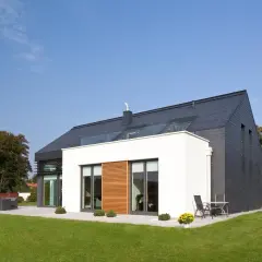 Nowoczesny dom z białymi tynkami mineralnymi i ciemnym dachem, otoczony zielonym ogrodem.