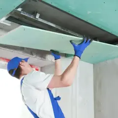 Pracownik montuje płyty gipsowo-kartonowe, tworząc zabudowę gk sufitu podwieszanego.