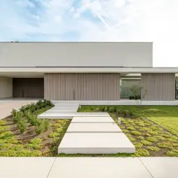 Nowoczesny dom z betonowym podjazdem i ścieżką z płyt. Świetny pomysł na wjazd do posesji, z minimalistyczną architekturą i zielenią.