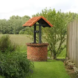 Urokliwa studnia w ogrodzie, otoczona zielenią i drewnianym płotem, zaprasza do odpoczynku.