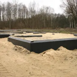 Fundament domu w piasku, zabezpieczony czarną folią jako izolacja przeciwwilgociowa.
