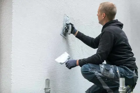 Murarz tworzy unikalne tynki strukturalne wzory na ścianie, nadając jej nowoczesny wygląd.