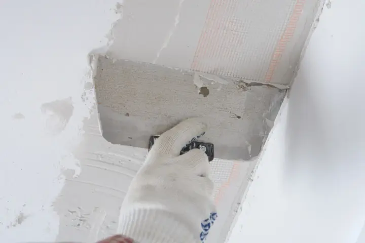Ręka w rękawicy nakłada zaprawę na styropian przy suficie, przygotowując do klejenia na piankę.