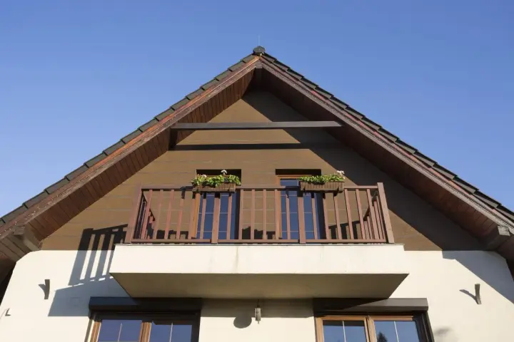 Montaż ciężkich elementów na elewacji domu, widok na dach i balkon z kwiatami.