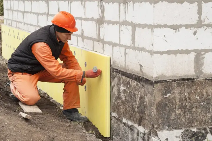 Budowlaniec montuje żółty styropian przy fundamencie. To ważny etap izolacji, który zapobiegnie przemarzaniu gruntu, np. pod przyszłym parkingiem.