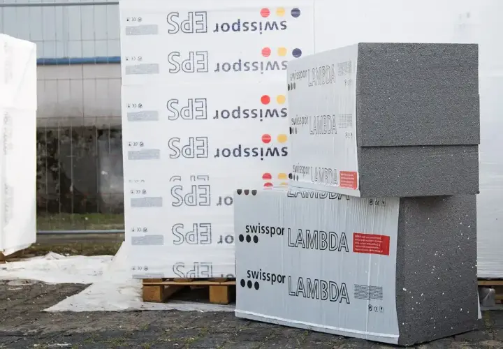 Stosy płyt izolacyjnych z napisem "swisspor LAMBDA" i "EPS" na paletach, gotowe do budowy.