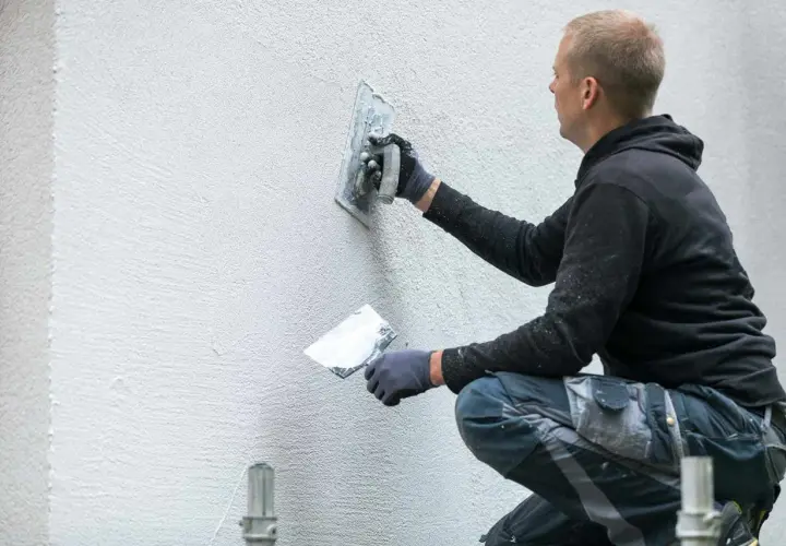 Murarz tworzy unikalne tynki strukturalne wzory na ścianie, nadając jej nowoczesny wygląd.