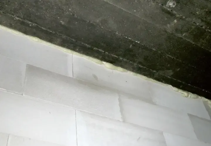 Piana montażowa wypełnia szczelinę między betonowym stropem a ścianą z białych pustaków. Idealne rozwiązanie, czym wypełnić dylatacje w ścianie.