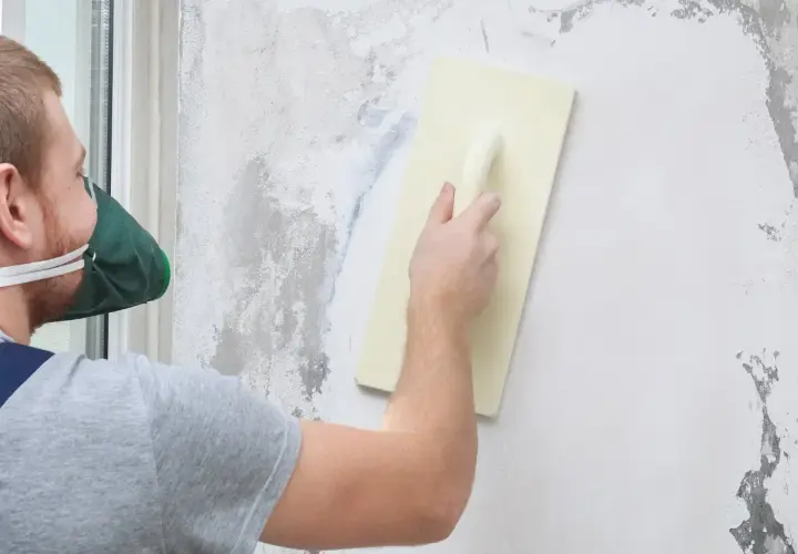 Pracownik w masce wygładza ścianę pacą. Ciekawi Cię, ile schnie tynk mozaikowy?