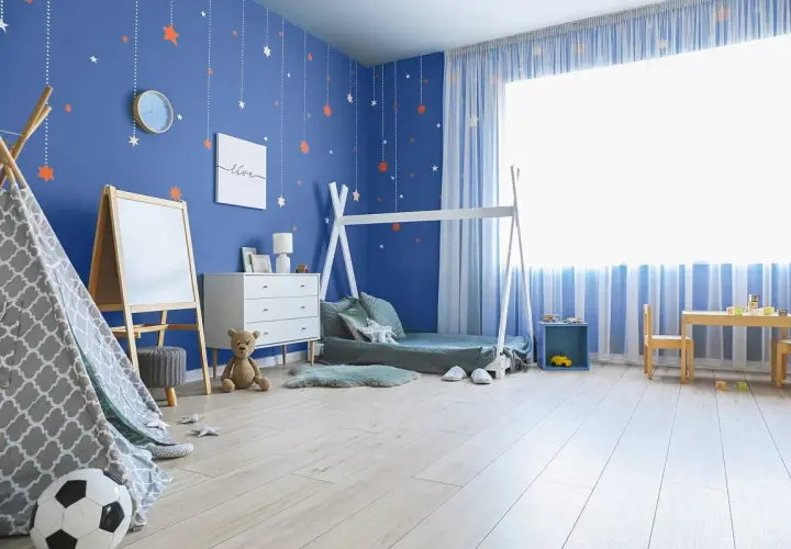 Pokój dziecka z niebieskimi ścianami i gwiazdkami. Inspiracje jak pomalować pokój dziecka: namiot tipi, łóżko domek, tablica, meble i stolik.