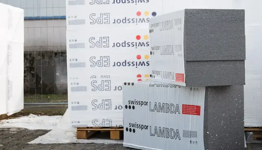 Stosy płyt izolacyjnych z napisem "swisspor LAMBDA" i "EPS" na paletach, gotowe do budowy.