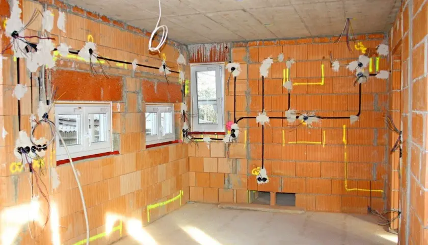 Rozprowadzona elektryka w nowym domu, widoczne przewody i puszki instalacyjne na ceglanych ścianach.