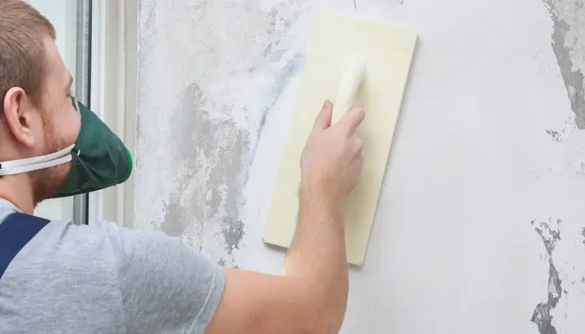 Pracownik w masce wygładza ścianę pacą. Ciekawi Cię, ile schnie tynk mozaikowy?