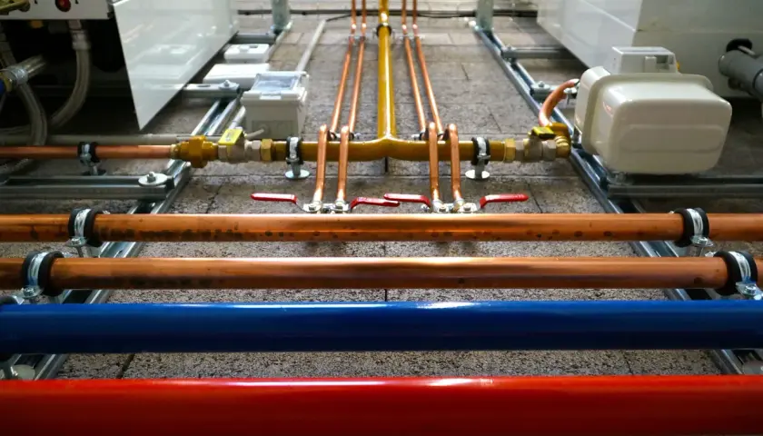 Instalacja hydrauliczna z miedzianymi rurami, zaworami i niebieską/czerwoną rurą. Ocieplenie rury wodnej jest kluczowe dla efektywności systemu.