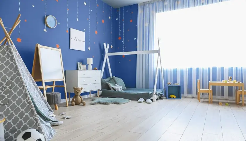 Pokój dziecka z niebieskimi ścianami i gwiazdkami. Inspiracje jak pomalować pokój dziecka: namiot tipi, łóżko domek, tablica, meble i stolik.