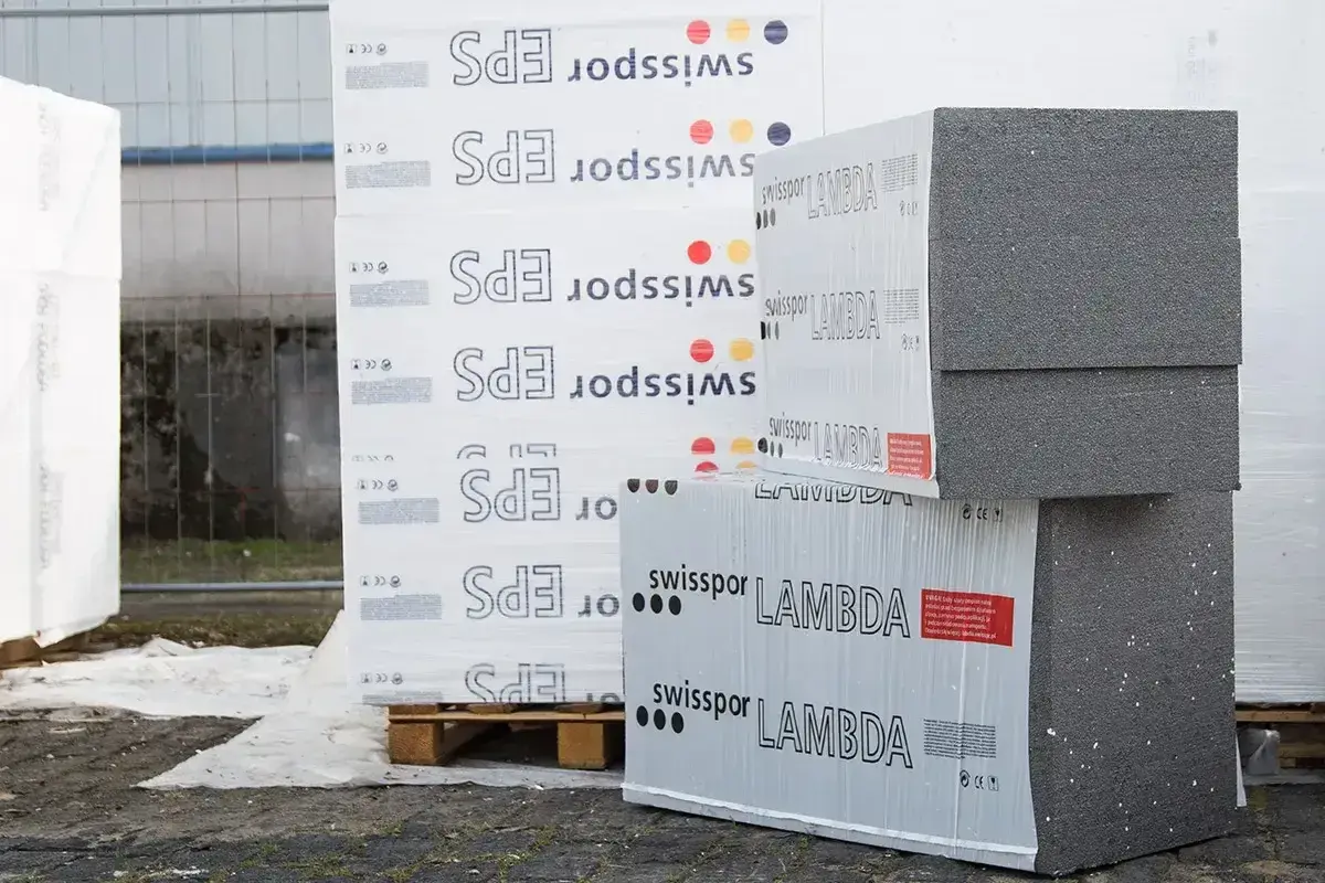 Stosy płyt izolacyjnych z napisem "swisspor LAMBDA" i "EPS" na paletach, gotowe do budowy.