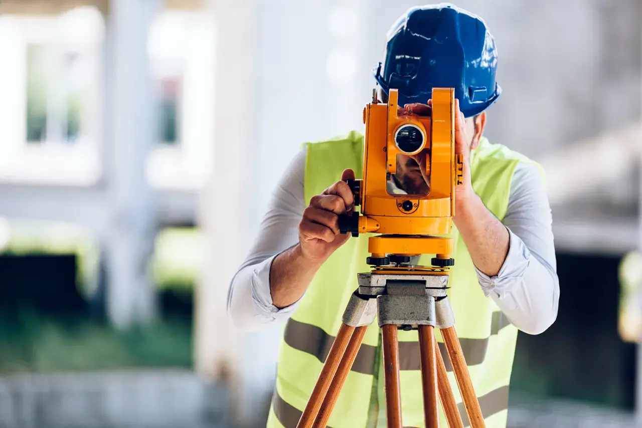 Geodeta w kasku i kamizelce odblaskowej pracuje z niwelatorem. Zastanawiasz się, ile kosztuje geodeta?