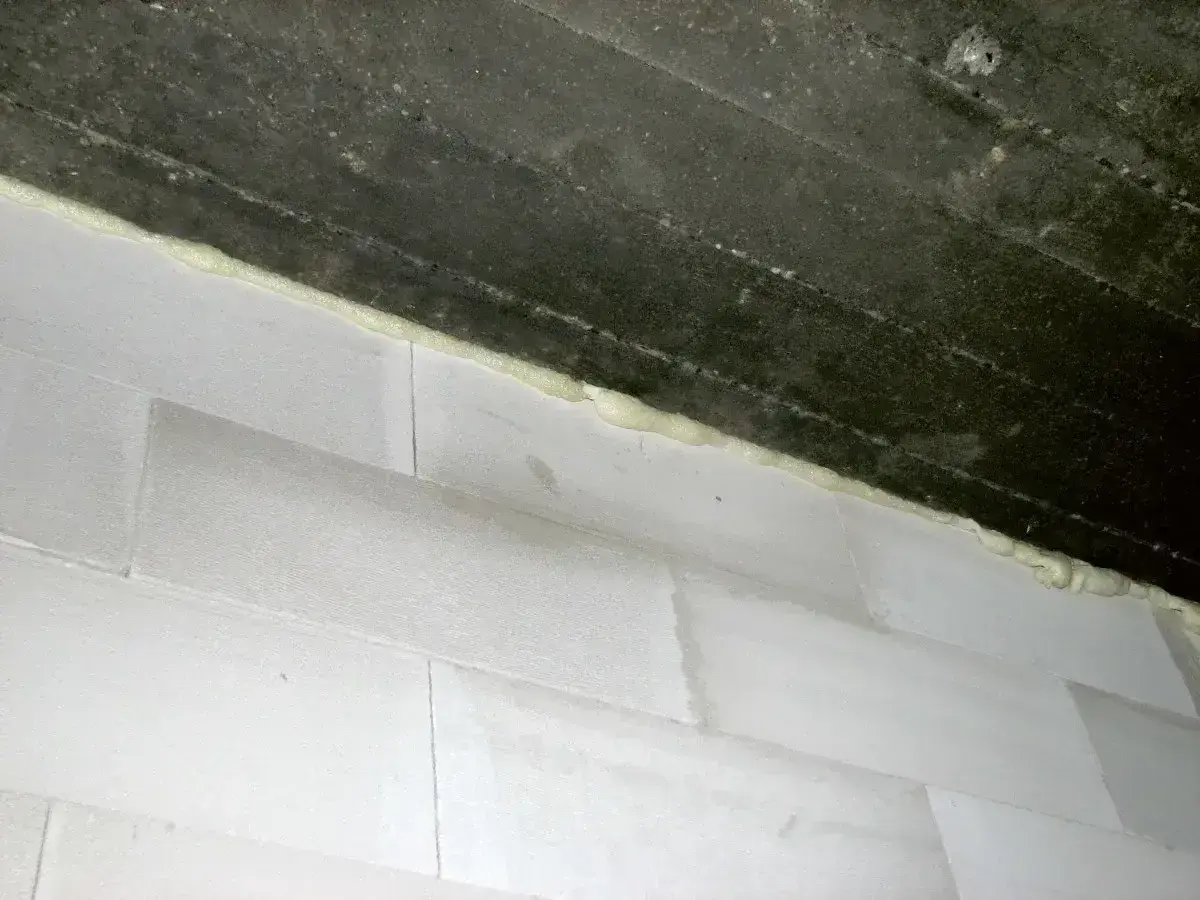 Piana montażowa wypełnia szczelinę między betonowym stropem a ścianą z białych pustaków. Idealne rozwiązanie, czym wypełnić dylatacje w ścianie.