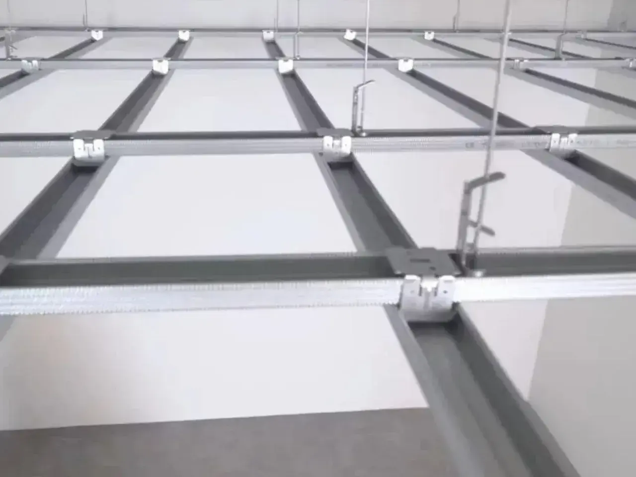 Sufit podwieszany krzyżowy z białymi panelami i metalową konstrukcją. Widać system profili, który tworzy siatkę, a nie pojedyncze belki.