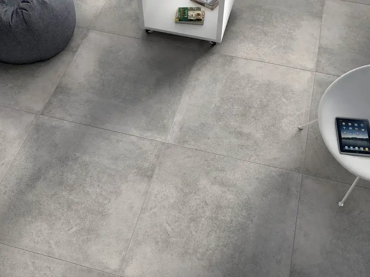 Nowoczesne wnętrze z szarymi, rektyfikowanymi płytkami na podłodze. Widać fragmenty mebli i tablet.