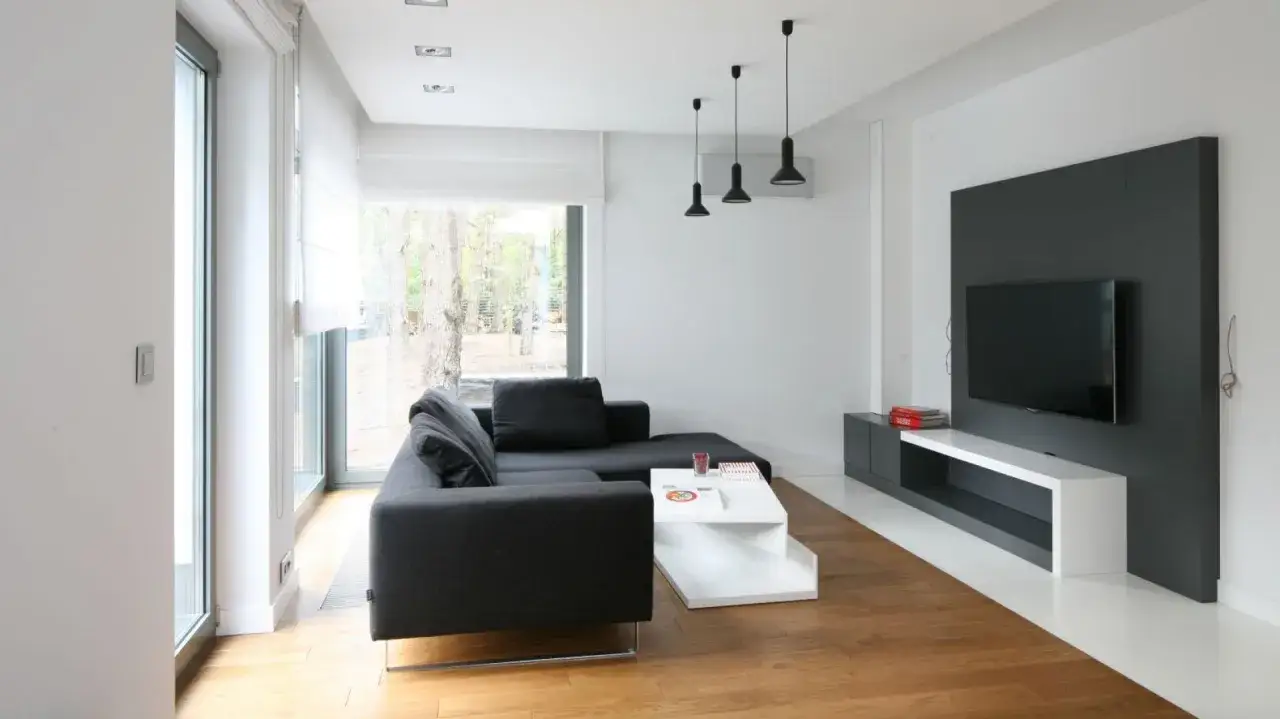 Nowoczesny salon z szarą kanapą i białym stolikiem. Dominują tu odcienie bieli, tworząc jasną i przestronną atmosferę.
