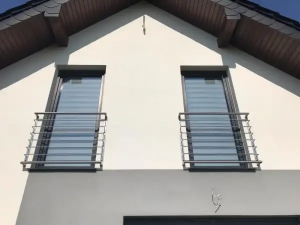 Nowoczesny montaż balkonu francuskiego na białej elewacji domu. Dwa okna z balustradami ze stali nierdzewnej.